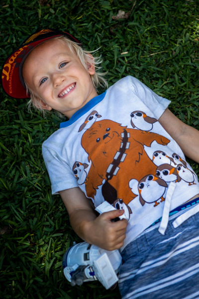 portrait of a boy laying in the grass with a star wars toy and shirt